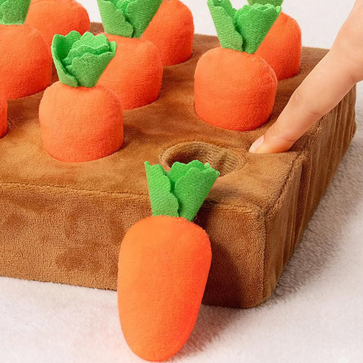 Hand pulling a plush carrot out of the snuffle mat pocket